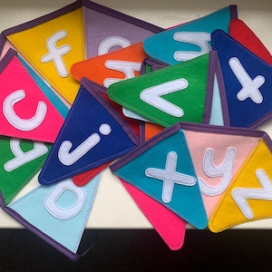 May include: A colorful felt alphabet banner with letters A through Z. Each letter is sewn onto a triangular flag with a purple border. The flags are arranged in a random order.