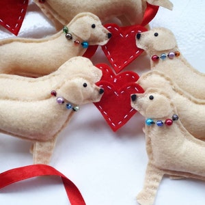 May include: Five felt dog ornaments with red hearts and beaded collars. The dogs are cream colored and have black eyes. The ornaments are perfect for a Valentine's Day theme.