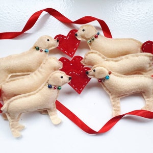 May include: Five felt golden retriever dog ornaments with red hearts and red ribbon. The dogs are wearing colorful beaded necklaces.