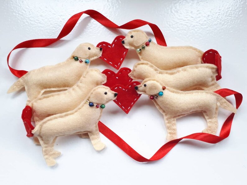 May include: Five felt golden retriever dog ornaments with red hearts and red ribbon. The dogs are wearing colorful beaded necklaces.