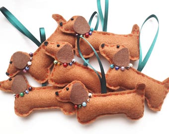 May include: Six brown felt dachshund ornaments with colorful beaded collars. The ornaments are hanging from green ribbon.