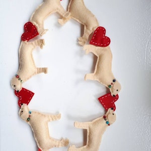 May include: A garland of six felt dogs with red felt hearts. Each dog has a beaded collar with colorful beads. The garland is tied with a red ribbon.
