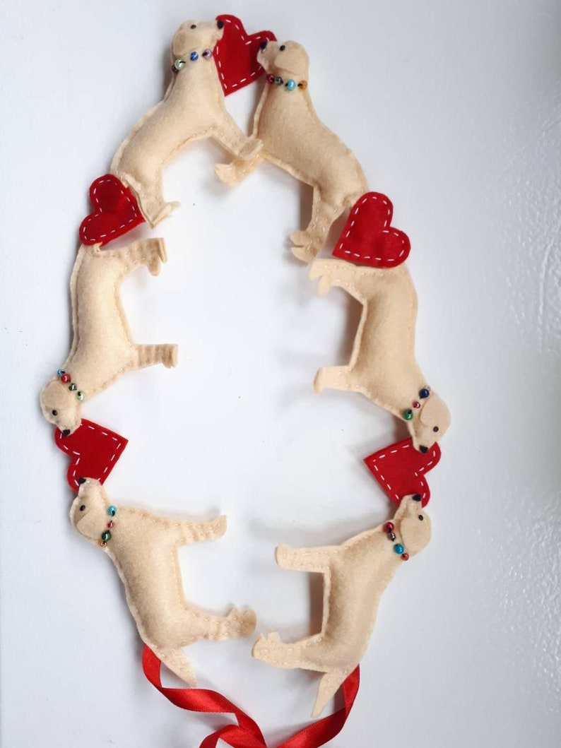 May include: A garland of six felt dogs with red felt hearts. Each dog has a beaded collar with colorful beads. The garland is tied with a red ribbon.