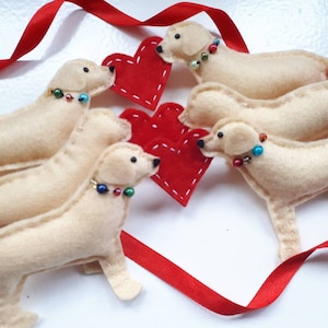 May include: Four felt golden retriever dog ornaments with red felt hearts. The dogs are arranged in a circle with their heads facing the center. Each dog has a beaded collar.