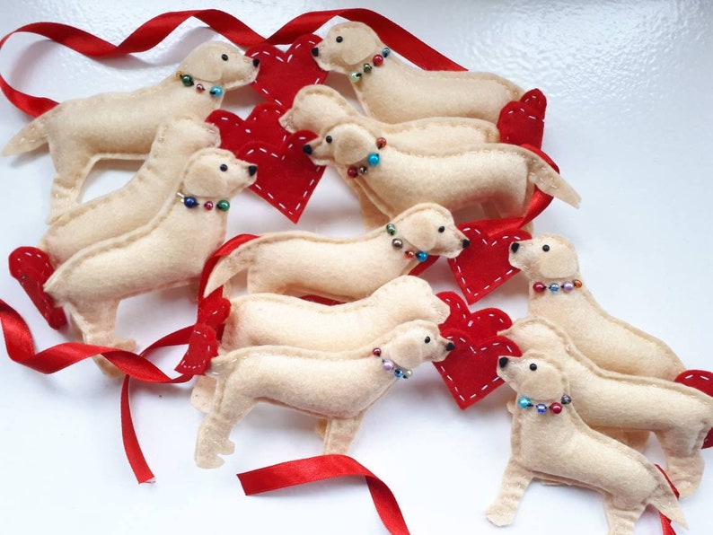 May include: A garland of felt golden retriever dog ornaments with red felt hearts. Each dog has a beaded collar with colorful beads.