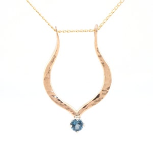 Puede incluir: Un collar de oro con un colgante martillado en forma de lágrima y una piedra preciosa azul.