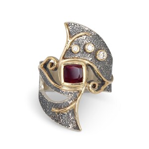 Peut inclure: Une bague en argent et or avec une pierre précieuse rouge et trois petits diamants. La bague a un design texturé et organique.