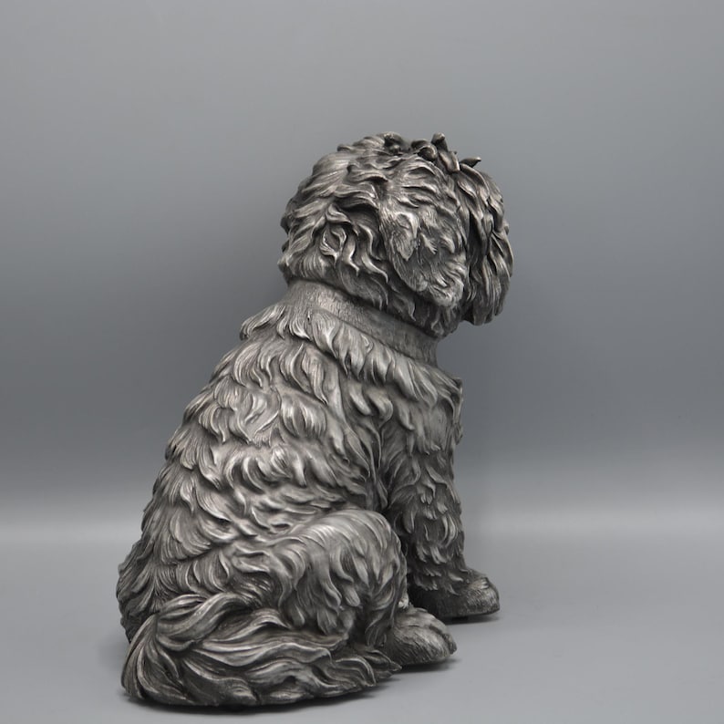 May include: A detailed, silver-colored dog statue in a seated position, facing away from the viewer. The sculpture features textured fur and a collar, showcasing a classic, elegant design. Ideal for home decor.
