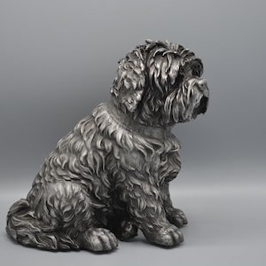 May include: A detailed silver-colored sculpture of a seated dog with a fluffy coat. The dog is depicted in a relaxed pose, with its head turned to the side. The sculpture has a textured surface, capturing the dog's fur and features.