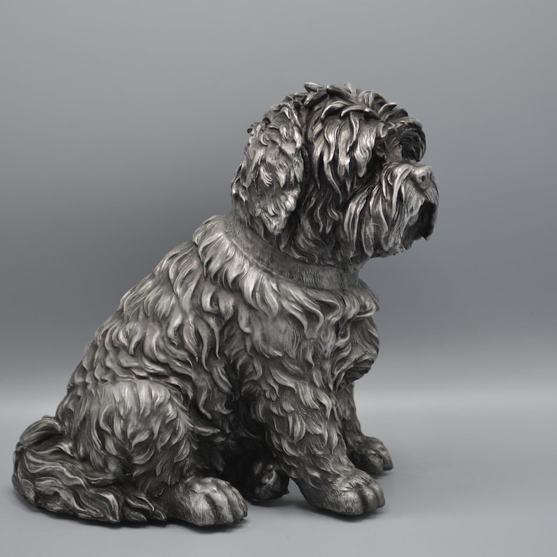 May include: A detailed silver-colored sculpture of a seated dog with a fluffy coat. The dog is depicted in a relaxed pose, with its head turned to the side. The sculpture has a textured surface, capturing the dog's fur and features.