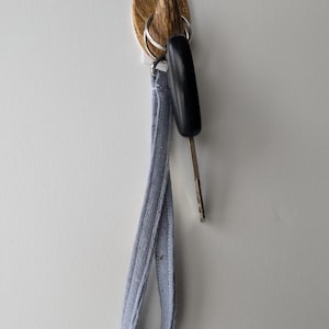 May include: A wooden wall hook with a key ring and a gray key chain attached. The hook is mounted on a white wall.