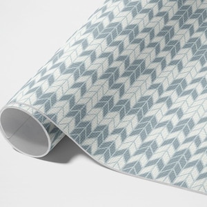 Op de afbeelding: Een rol blauw en wit gestreept cadeaupapier met een geometrisch ontwerp. Het papier is opgerold en het uiteinde is zichtbaar.