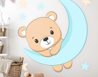May include: A light blue crescent moon with a brown teddy bear sitting on it. The moon and bear are surrounded by small yellow and blue stars.