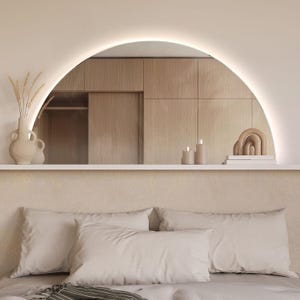 May include: A bedroom with a white headboard and a large arched mirror above a bed with white bedding and pillows. The mirror reflects a wooden closet with a sliding door.