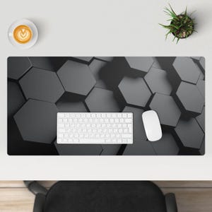 Op de afbeelding: Een zwart-witte bureau mat met een geometrisch patroon van zeshoeken. Een wit toetsenbord en een witte muis liggen op de mat.