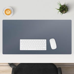 May include: A gray desk mat with a white keyboard and a white mouse on top of it. The desk mat is on a white desk.