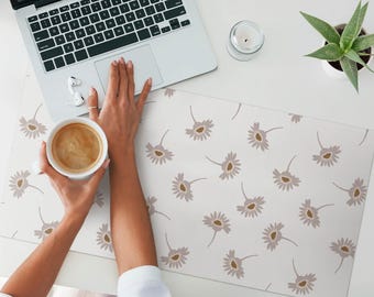 Puede incluir: Una alfombrilla de escritorio blanca con un patrón repetitivo de flores estilizadas de color marrón claro y gris. Una mano sostiene una taza blanca llena de café.