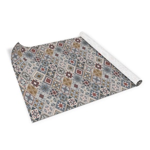 Op de afbeelding: Een decoratief, gepatroneerd inpakpapier met een herhalend ontwerp van blauwe, rode, bruine en witte tegels. Het papier is opgerold en het uiteinde is opgerold.