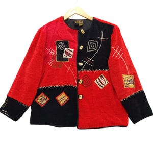 May include: A red and black jacket with geometric embroidery and gold-colored buttons. The jacket features a split design with one side red and the other black. The embroidery includes squares, spirals, and linear patterns. The jacket is hanging on a wooden hanger.