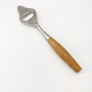 May include: A bottle opener with a stainless steel head and a wooden handle. The opener has a teardrop-shaped head with a circular opening. The handle is made of light brown wood.
