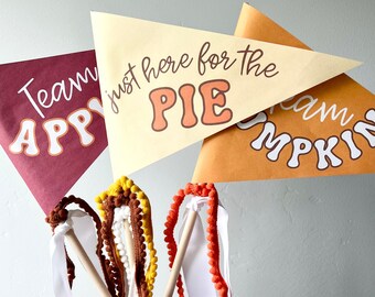 May include: Thanksgiving-themed pennant banners with text that reads "Team Happy", "just here for the PIE", and "Cream Pumpkin". The image also shows decorative wands with pom-poms and ribbons in fall colors.