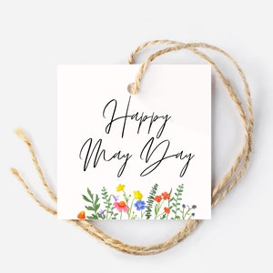 Puede incluir: Etiqueta de regalo blanca con el texto "Happy May Day" en fuente de letra cursiva negra. La etiqueta está decorada con una fila de flores coloridas y hojas verdes en la parte inferior.
