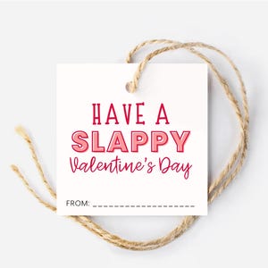 May include: A white square gift tag with the text "HAVE A SLAPPY Valentine's Day" in red and pink lettering. The tag is tied with a natural twine string, and has a space to write "FROM:" on the bottom.