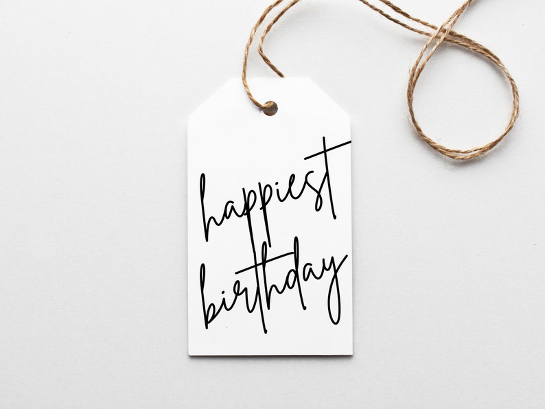 May include: A white gift tag with the words "happiest birthday" in black script. The tag is attached to a brown twine string, set against a white background. The tag is a simple, elegant design.