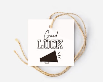 May include: A white gift tag with black text that reads "Good LUCK" with a black megaphone graphic below. The tag is tied with twine.