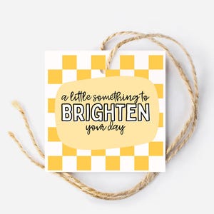 May include: A yellow and white checkered gift tag with a yellow speech bubble that says "a little something to BRIGHTEN your day".