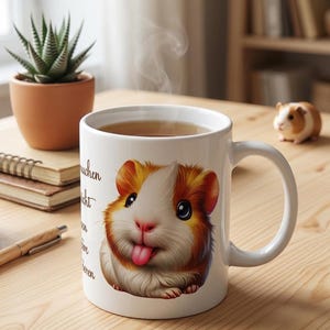 Könnte beinhalten: Weiße Keramiktasse mit einer Cartoon-Meerschweinchen-Illustration in Orange-, Braun- und Weißtönen, die ihre Zunge herausstreckt. Die Tasse enthält ein heißes Getränk und hat einen gebogenen Griff. Text ist auf der Seite aufgedruckt. Eine kleine Meerschweinchen-Figur befindet sich im Hintergrund.