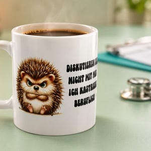 Könnte beinhalten: Eine weiße Keramiktasse gefüllt mit schwarzem Kaffee, bedruckt mit einem wütenden braunen Igel mit verschränkten Armen. Der schwarze Text auf der Seite der Tasse lautet: DISKUTIEREN SIE NICHT MIT MIR ICH KASTRIERE BERUFLICH.