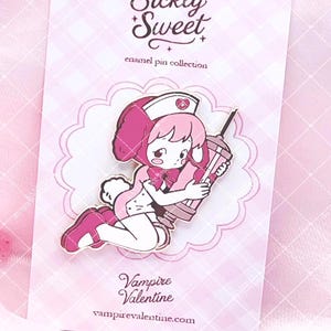 May include: A metal enamel pin featuring a cartoon character dressed as a nurse with pink hair and bunny ears, holding a large syringe. The pin is attached to a light pink checkered backing card with the text Sickly Sweet enamel pin collection.