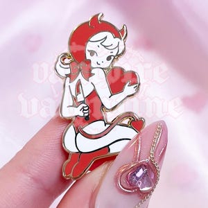 Op de afbeelding: Gouden emaille pin met een cartoonfiguur met rode hoorns, een rode jurk en een rood hart. Het figuur houdt het hart in zijn linkerhand en heeft een duivelsstaart.