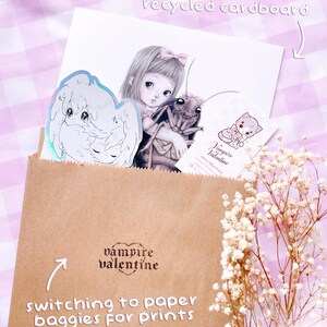 a brown paper bag with a sticker, a drawing of a girl, and some flowers. The bag is labeled "switch to paper bags for prints" and "vampire valentine".