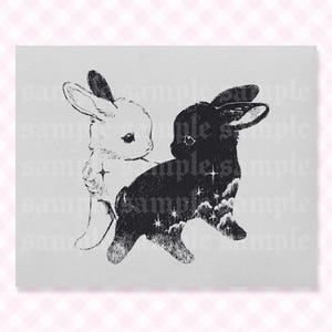 May include: A black and white illustration of two rabbits standing back to back. The left rabbit is white with fine line details, while the right rabbit is black with a starry night sky pattern featuring clouds and four-pointed stars inside its body.