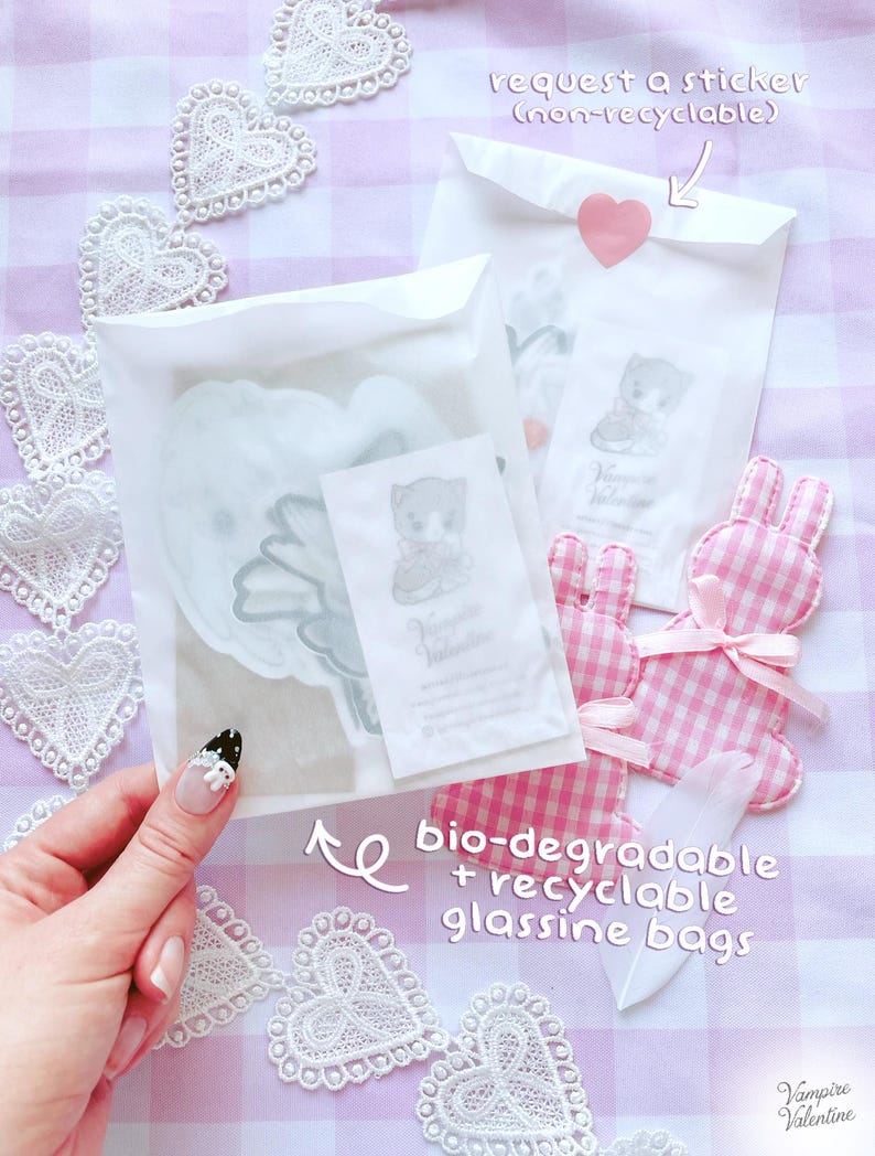 A hand holding a clear plastic bag with a heart-shaped cutout, surrounded by lace doilies and a pink and white checkered bunny plush toy.