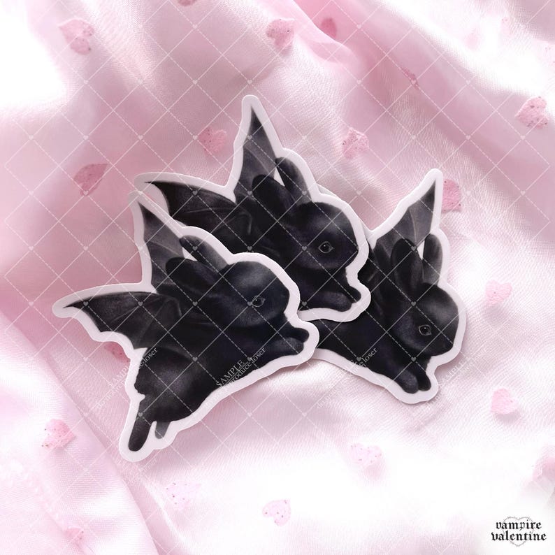 May include: Three die-cut stickers featuring black rabbits with bat wings. Each sticker shows a dark-furred bunny with pointed ears and leathery wings extended. The stickers have a white border and include the text SAMPLE printed on the surface.