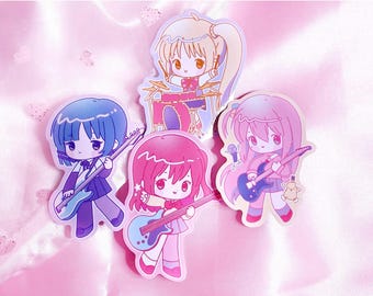 May include: Four die-cut stickers featuring chibi-style characters playing musical instruments. One character plays drums, while three others play electric guitars. The characters have large eyes and colorful hair in shades of blue, pink, and blonde.
