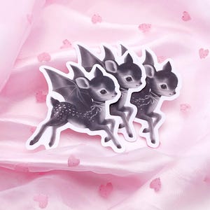 May include: Three stickers featuring a black and white illustration of a deer with bat wings. The stickers are on a pink, heart-patterned fabric. The text "Vampire by Valentine" is in the bottom right corner.