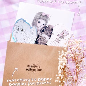 a brown paper bag with a sticker, a drawing of a girl, and some flowers. The bag is labeled "switch to paper bags for prints" and "vampire valentine".