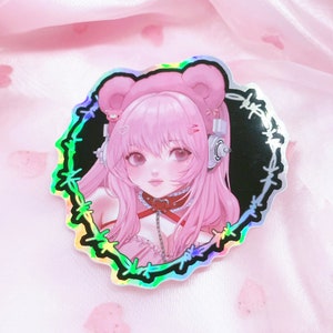 May include: A holographic sticker featuring a pink-haired anime character with bear ears, wearing a choker and headphones. The character is surrounded by a black barbed wire border.