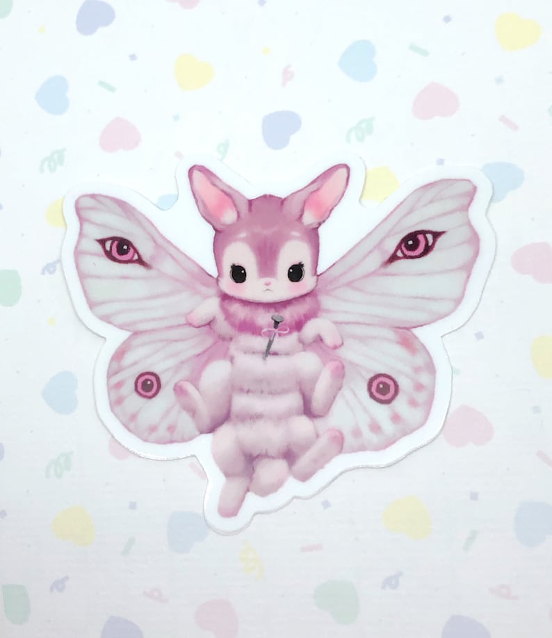May include: A pink and white moth with large eyes and a fuzzy body. The moth has a pink rabbit head and is holding a pink flower.