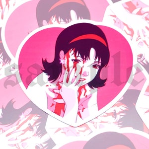 Op de afbeelding: Een roze sticker in de vorm van een hart met een cartoonafbeelding van een vrouw met zwart haar en een rood hoofdband. De vrouw heeft bloed op haar gezicht en handen.