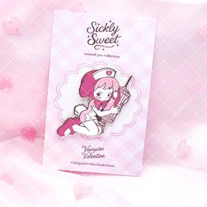 May include: An enamel pin on a light pink checkered backing card featuring the text Sickly Sweet enamel pin collection and Vampire Valentine. The pin depicts a cartoon character with pink hair wearing a nurse hat and holding a large syringe.