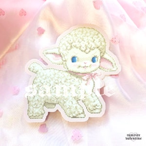 May include: A white lamb sticker with blue eyes and a pink bow. The lamb is standing on a pink background with white hearts.