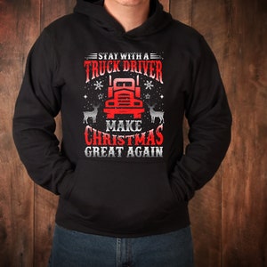 May include: Black hooded sweatshirt with a red and white graphic design featuring a semi-truck, reindeer, and the text "Stay with a truck driver make Christmas great again."
