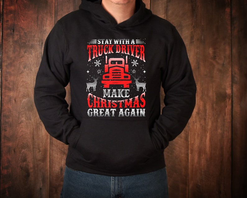 May include: Black hooded sweatshirt with a red and white graphic design featuring a semi-truck, reindeer, and the text "Stay with a truck driver make Christmas great again."