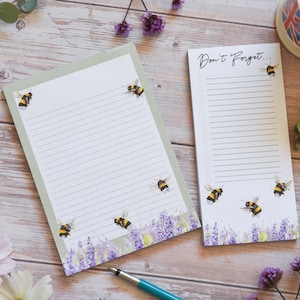 May include: Two notepad sets with lined paper and a bee theme. The larger notepad has a green border and says "Don't Forget..." on the top. Both notepads have a lavender and bee design at the bottom.
