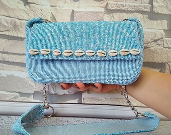 May include: A light blue beaded handbag with a chain strap and a row of white seashells across the front.
